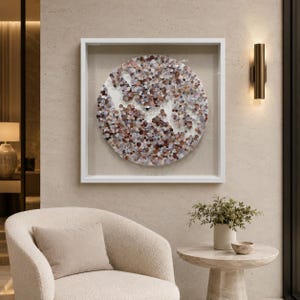 May include: A square white shadow box frame containing a circular wall art piece composed of numerous small, overlapping circular discs in shades of brown, copper, silver, and white, arranged to create a textured, multi-layered abstract pattern.