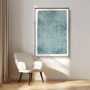 May include: Teal and white abstract art print in a gold frame. The artwork features a grid-like pattern with curved lines, creating a textured effect. The print is displayed on a white wall above a white armchair with dark wooden legs, creating a modern interior design.