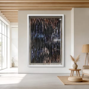 Könnte beinhalten: Abstrakte Wandkunst in einem weißen Rahmen. Das Kunstwerk zeigt vertikale Streifen in Schwarz-, Braun- und Blautönen, die einen strukturierten, geschichteten Effekt erzeugen. Das Stück wird in einem modernen, hellen Raum mit neutralen Tönen ausgestellt.