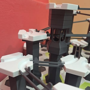 May include: A close-up of a marble run toy set. The set features black and white towers, tracks, and supports. The marble run is constructed of plastic and is designed for children to build and play with.