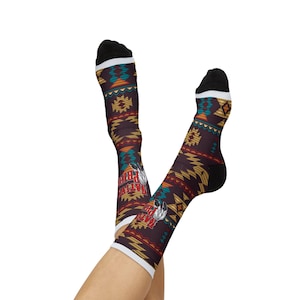 May include: A pair of socks with a Native American-inspired design. The socks feature a dark brown base with geometric patterns in teal, orange, and yellow. The text "Native Pride" is visible, along with a feather graphic. The socks have black heels and toes, and white cuffs.