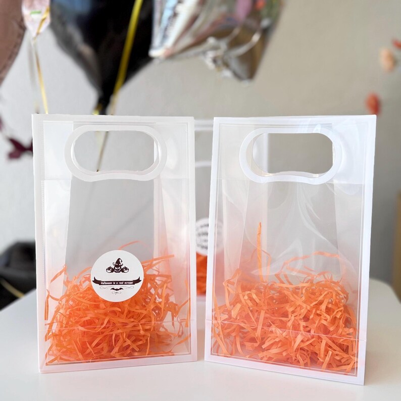 Peut inclure: Deux sacs cadeaux en plastique transparent avec une poign&eacute;e, remplis de papier d&eacute;chiquet&eacute; orange. Chaque sac a une bordure blanche et un autocollant circulaire avec un motif sur le th&egrave;me d'Halloween et le texte "Halloween is a real scream!"