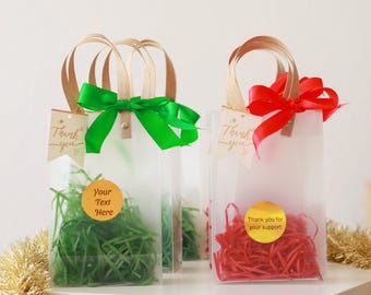 May include: Clear gift bags with brown handles, green and red ribbon bows, and tags that say "Thank you". The bags contain green and red shredded paper and round stickers that say "Your Text Here" and "Thank you for your support".
