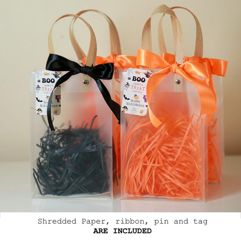 May include: Clear plastic Halloween treat bags filled with black and orange shredded paper. Each bag has a ribbon bow and a tag that reads "BOO Here's a TREAT for you HAPPY HALLOWEEN". The bags have wooden handles.