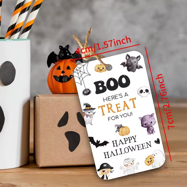May include: A white Halloween gift tag, 7cm tall and 4cm wide, with the text "BOO HERE'S A TREAT FOR YOU! HAPPY HALLOWEEN". The tag is decorated with Halloween-themed illustrations, including bats, pumpkins, and ghosts.