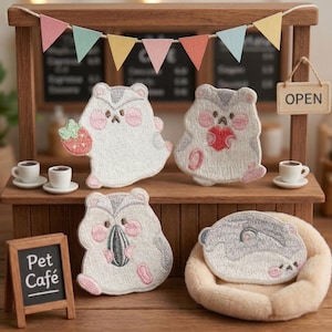 May include: A miniature wooden cafe scene featuring four embroidered hamster patches. One hamster holds a strawberry, another a heart, a third a sunflower seed, and the last rests on a bed. A sign reads "Pet Cafe."