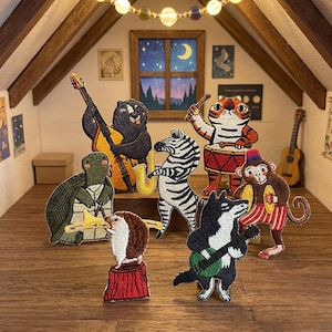Pode incluir: Uma cena fantástica com patches bordados de animais músicos num sótão acolhedor. Um urso toca contrabaixo, uma zebra saxofone e um tigre bateria. Outros animais incluem uma tartaruga, um ouriço, um macaco e um lobo com uma guitarra.