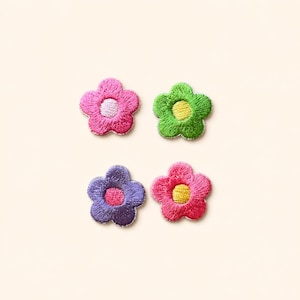 May include: Four embroidered flower patches arranged in a square grid. The top left is hot pink with a light pink center, the top right is lime green with a yellow center, the bottom left is purple with a pink center, and the bottom right is red with a yellow center.