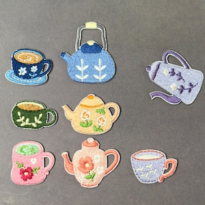 Könnte beinhalten: Eine Sammlung von gestickten Aufnähern mit Teetassen und Teekannen in verschiedenen Farben. Die Aufnäher zeigen eine blaue Teetasse mit weißen Blumen, eine grüne Teetasse mit Blattmotiven und eine rosa Teetasse mit einer roten Blume. Die Teekannen sind blau, gelb und rosa.