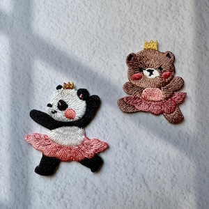 May include: Two embroidered patches: a panda and a bear, both wearing pink tutus and gold crowns. The panda is black and white, while the bear is brown. Both have rosy cheeks and are in a dancing pose.