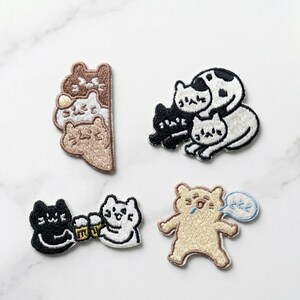 May include: Four embroidered cat patches. One shows stacked brown cats, another a black and white cat pair, a third depicts cats toasting beer, and the last shows a sleepy cat with a thought bubble. Ideal for clothing.