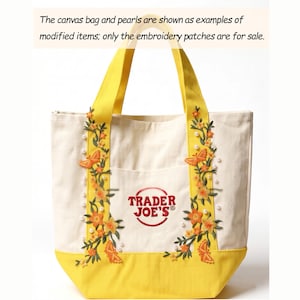 Könnte beinhalten: Cremefarbene Canvas-Tragetasche mit gelbem Boden und Henkeln. Sie hat gestickte orangefarbene und gelbe Blumen- und Schmetterlingsdesigns mit Perlenakzenten. Das Trader Joe's-Logo ist auf der Vorderseite zu sehen. Der Text lautet: 'Die Canvas-Tasche und die Perlen werden als Beispiele für modifizierte Artikel gezeigt; nur die Stickereiflicken stehen zum Verkauf.'