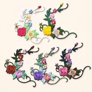 May include: Five embroidered floral corner patches featuring intricate rose and leaf designs. The patches display various color combinations including pink, yellow, purple, blue, and green threads on curved stems, arranged in a decorative arc pattern.