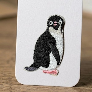 Può includere: Toppa ricamata a forma di pinguino con corpo nero, petto bianco e piedi rosa. Il pinguino ha un design cucito dettagliato, con testa nera e viso bianco. La toppa è probabilmente per abbigliamento o accessori.