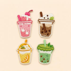 May include: Four embroidered patches shaped like beverage cups. One is pink with a cherry, one is brown with boba pearls, one is yellow with an orange slice, and one is green with boba pearls. Each cup features a straw and whipped cream topping.