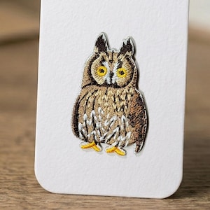 May include: Embroidered owl patch with brown, tan, and white thread. The owl has yellow eyes and a detailed feather design. The patch is on a white background.