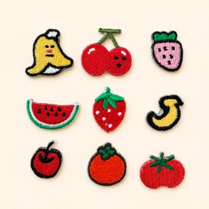 Può includere: Una collezione di nove toppe ricamate a forma di frutta e verdura, tra cui una banana gialla, ciliegie rosse, una fragola rosa, una fetta di anguria, una fragola rossa, una mezzaluna gialla, una ciliegia rossa, un pomodoro arancione e un pomodoro rosso.