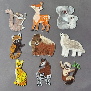 Puede incluir: Nueve parches bordados de animales, incluyendo una ardilla, un ciervo, koalas, un panda rojo, un mamut, un lobo, un serval, un okapi y un perezoso. Los parches presentan costuras detalladas y varios colores, como marrón, naranja, amarillo y gris.