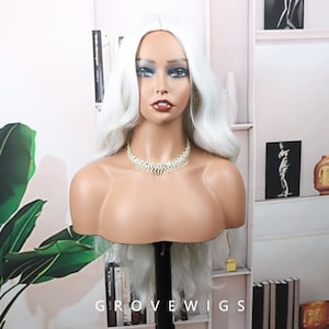Puede incluir: Una cabeza de maniquí que muestra una larga peluca blanca y ondulada. La peluca está peinada con una raya a un lado y rizos sueltos. El maniquí lleva un collar brillante. El texto "GROVEWIGS" es visible en la parte inferior de la imagen.