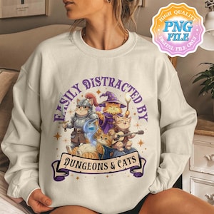 May include: Cream-colored sweatshirt featuring a graphic of cartoon cats dressed as fantasy characters. The design includes a knight cat, a wizard cat, and a cat playing a guitar, with the text "Easily Distracted By Dungeons & Cats."