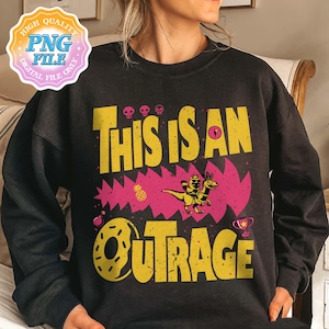 May include: Black sweatshirt with a yellow and pink graphic. The graphic reads "THIS IS AN OUTRAGE" in a distressed font. The design includes a dinosaur riding another dinosaur, skulls, a pineapple, a donut, and a trophy.