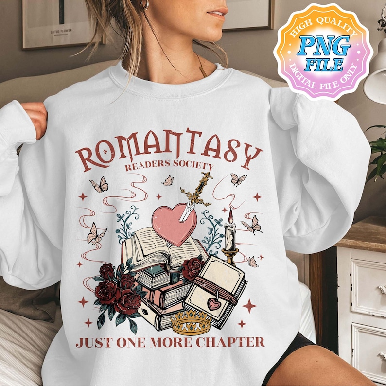May include: White sweatshirt with a graphic design featuring a stack of books, a heart with a sword through it, a candle, and butterflies. The text reads "Romanstasy Readers Society" and "Just One More Chapter".