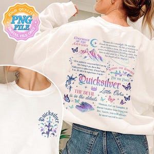 May include: White sweatshirt with a colorful graphic print featuring the text "Quicksilver" and "The Devil is in the details". The graphic also includes a mountain range, butterflies, and a sword. The text "Kingfisher of the Ajun Gate" is printed at the top of the graphic.