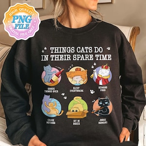 May include: Dark grey sweatshirt featuring the phrase "THINGS CATS DO IN THEIR SPARE TIME" and cat illustrations. The illustrations show cats knocking things over, sleeping, demanding food, chasing nothing, sitting in boxes, and judging humans.