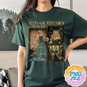 May include: Dark green t-shirt with a fantasy art design. The design includes the text "Aelin Galathynius Fireheart" and two illustrations of a woman with long blonde hair. One illustration shows the woman in a green dress, and the other shows her with a deer.