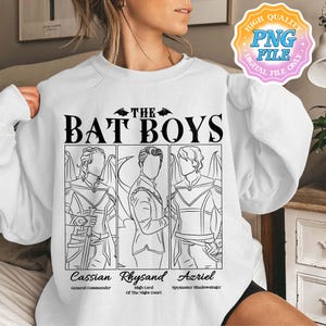 Op de afbeelding: Een wit T-shirt met een zwarte afbeelding van drie mannen met vleugels. De tekst "THE BAT BOYS" staat boven de afbeelding. De namen "Cassian", "Rhysand" en "Azriel" staan onder de afbeelding, samen met hun titels: "General Commander", "High Lord of the Night Court" en "Spymaster Shadowsinger".
