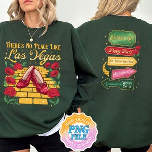 May include: Dark green sweatshirt with the text "THERE'S NO PLACE LIKE Las Vegas" and a graphic of ruby red shoes on a yellow brick road. The back of the sweatshirt features directional signs for Emerald City, Poppy Field, and Witch's Castle.