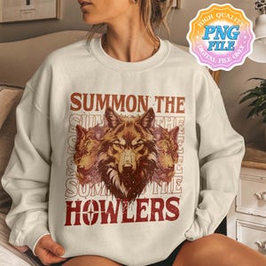 May include: Cream-colored sweatshirt featuring a graphic of three wolf heads in shades of brown and red. The text "SUMMON THE HOWLERS" is printed above and below the wolf illustration in a distressed, vintage style.