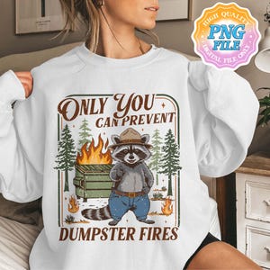 May include: White sweatshirt with a graphic featuring a raccoon in a park ranger hat, standing in front of a dumpster fire. The text reads "Only You Can Prevent Dumpster Fires."