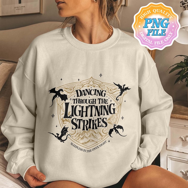 May include: Cream-colored sweatshirt with a graphic design featuring the text "Dancing Through The Lightning Strikes" in a stylized font. The design includes black silhouettes of dragons and a mountain landscape. The phrase "Sleepless in the Onyx Night" is also present.
