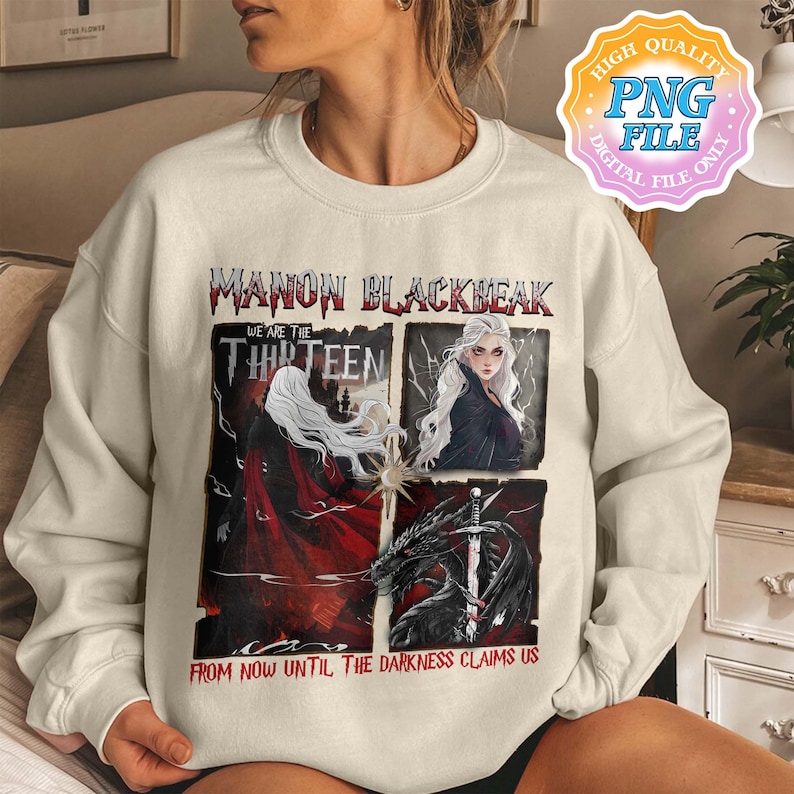 May include: A white sweatshirt with a graphic print of a woman with long white hair and a black cape. The text on the graphic reads "Manon Blackbeak, We are the Thirteen, From now until the darkness claims us".