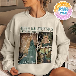 May include: A cream-coloured sweatshirt with a fantasy graphic. The design features the text "AELIN GALATHYNIUS FIREHEART" and illustrations of two women and a stag. The graphic uses shades of green, brown, and gold.