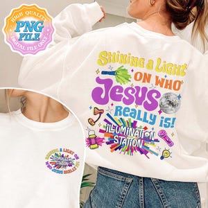 May include: White sweatshirt with the text "Shining a Light on Who Jesus Really is!" in colorful lettering. The design includes a disco ball, a flashlight, and other illustrations. A smaller version of the design is on the front.
