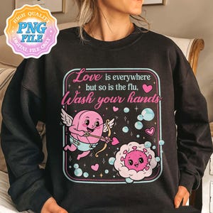 May include: Black sweatshirt with a graphic design featuring a pink cupid with a bow and arrow, a cartoon virus, and the text "Love is everywhere but so is the flu, Wash your hands."