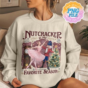 Puede incluir: Sudadera color crema con un gráfico temático de El Cascanueces. El diseño incluye una bailarina con tutú rosa, un soldado Cascanueces, un árbol de Navidad y el texto "Nutcracker is my favorite season."