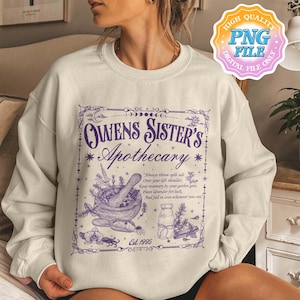 Puede incluir: Sudadera color crema con un diseño gráfico púrpura. El diseño presenta el texto "Owens Sister's Apothecary" con ilustraciones de un mortero y una maja, hierbas y una botella. También se incluye el texto "Est. 1995".