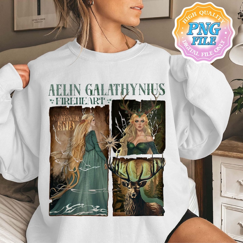 May include: White sweatshirt with a fantasy graphic. The design features the text "AELIN GALATHYNIUS FIREHEART" and illustrations of a woman in a green dress and a deer with antlers. The graphic uses green, brown, and gold colours.