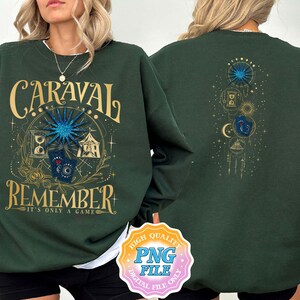 May include: A dark green sweatshirt with the text "Caraval Remember It's Only A Game" in gold lettering. The front of the sweatshirt features a graphic design with a blue star, a tent, and other symbols. The back of the sweatshirt features a graphic design with a blue star, a crescent moon, and other symbols.