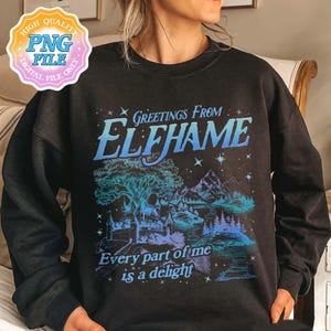 K&ouml;nnte beinhalten: Schwarzer Pullover mit einem blauen und wei&szlig;en Grafikdruck einer Fantasielandschaft mit einem Baum, Bergen und einem Schloss. Der Text "Greetings from Elfhame" und "Every part of me is a delight" ist auf dem Shirt gedruckt.