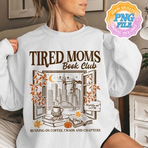 Op de afbeelding: Witte sweatshirt met een afbeelding met de tekst "TIRED MOMS Book Club". Het ontwerp toont een open raam met een skyline, boeken, een koffiekopje en de tekst "RUNNING ON COFFEE, CHAOS AND CHAPTERS". Alleen een digitale bestand.