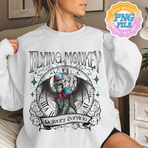 Puede incluir: Sudadera blanca con un diseño de un mono alado con sombrero y capa, con la frase "Flying Monkey Delivery Service". El diseño incluye una esfera de reloj y estrellas, con una estética vintage.