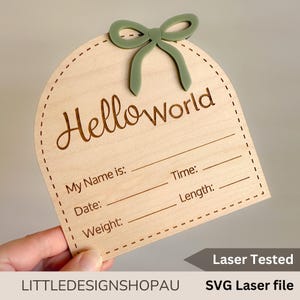 Puede incluir: Un letrero de madera con un lazo verde en la parte superior. El letrero dice "Helloworld" y tiene espacios para rellenar el nombre del bebé, la fecha, el peso, la hora y la longitud. El letrero está cortado con láser y viene con un archivo SVG.