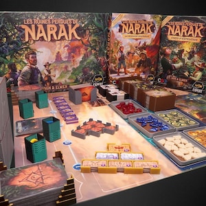 Peut inclure: Jeu de société "Les Ruines Perdues de Narak" avec des pièces de jeu, des cartes et des boîtes. Le plateau de jeu présente divers composants dans des plateaux, notamment des pièces rouges, bleues et beiges. Les boîtes présentent des illustrations d'explorateurs.