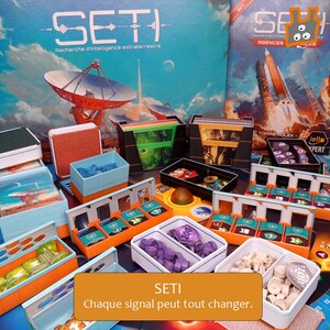 Peut inclure: Le jeu de société SETI comprend une grande boîte illustrée d'une antenne parabolique, plusieurs organisateurs de cartes en plastique orange, bleu et noir, ainsi que divers jetons de jeu violets, blancs et verts, et une boîte avec une fusée.