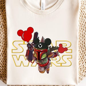 May include: A white t-shirt with a graphic of a Star Wars Boba Fett character wearing a Mickey Mouse hat and holding a red balloon. The text "STAR WARS" is printed in gold below the character.