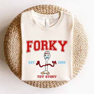 May include: A white ceramic mug with a black handle and the text "But First, Coffee" in a bold, black font. The mug is set against a blurred background, suggesting a cozy setting.